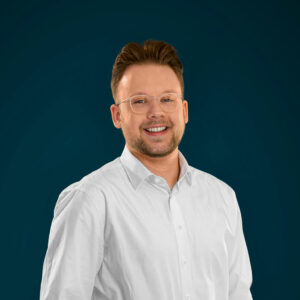 Philipp Zahnow von Rocket Floor im weißen Hemd vor blauem Hintergrund.